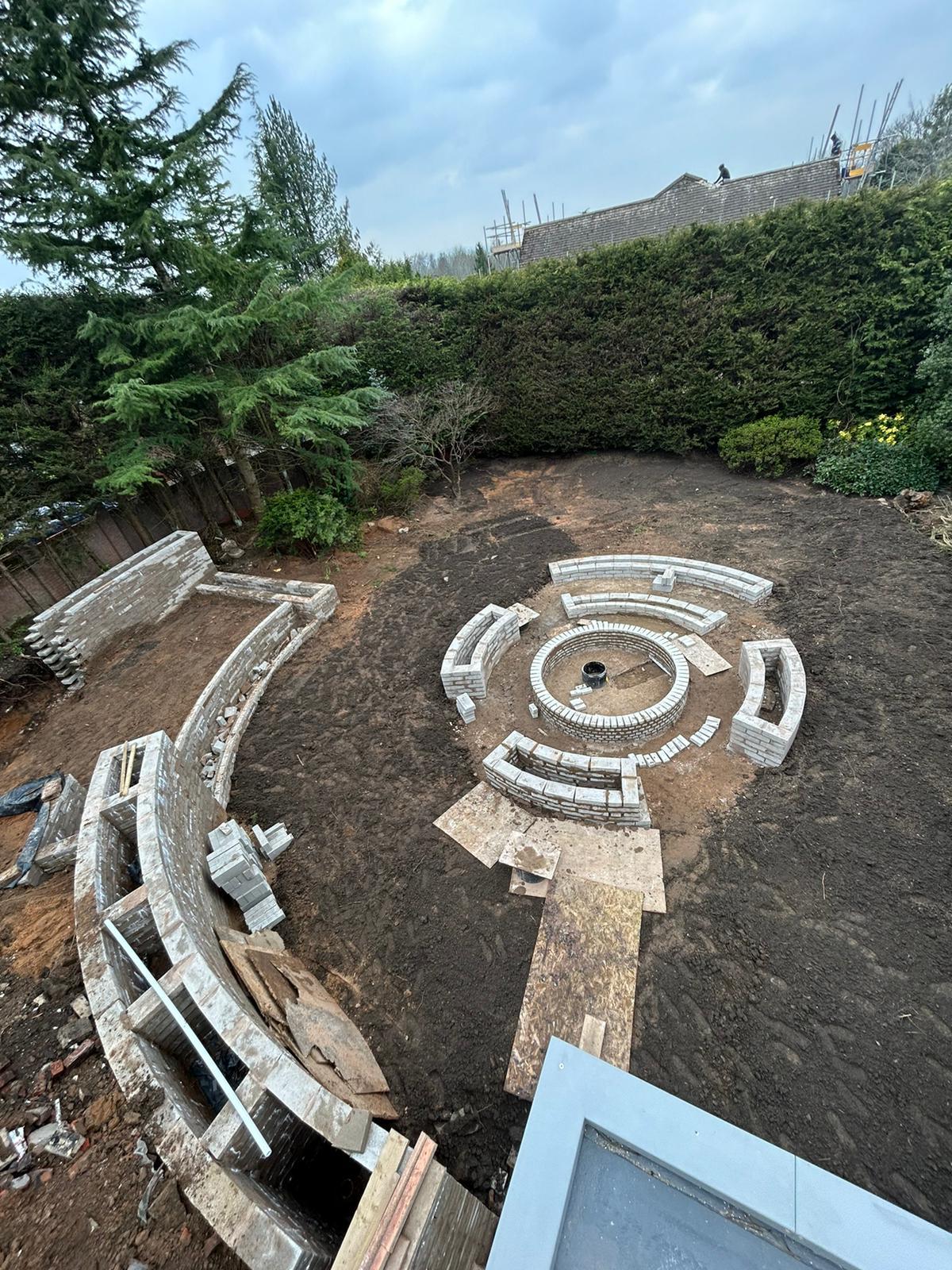 Circular garden feature under construction, block walls being built around a sunken firepit