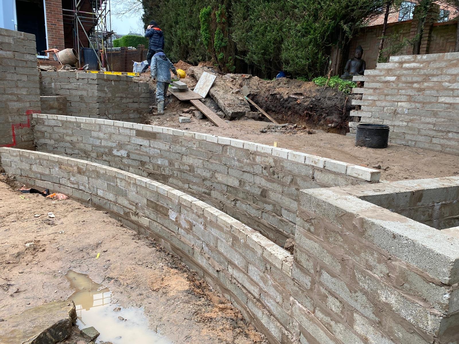 Curved retaining wall under construction ahead of a circular garden build