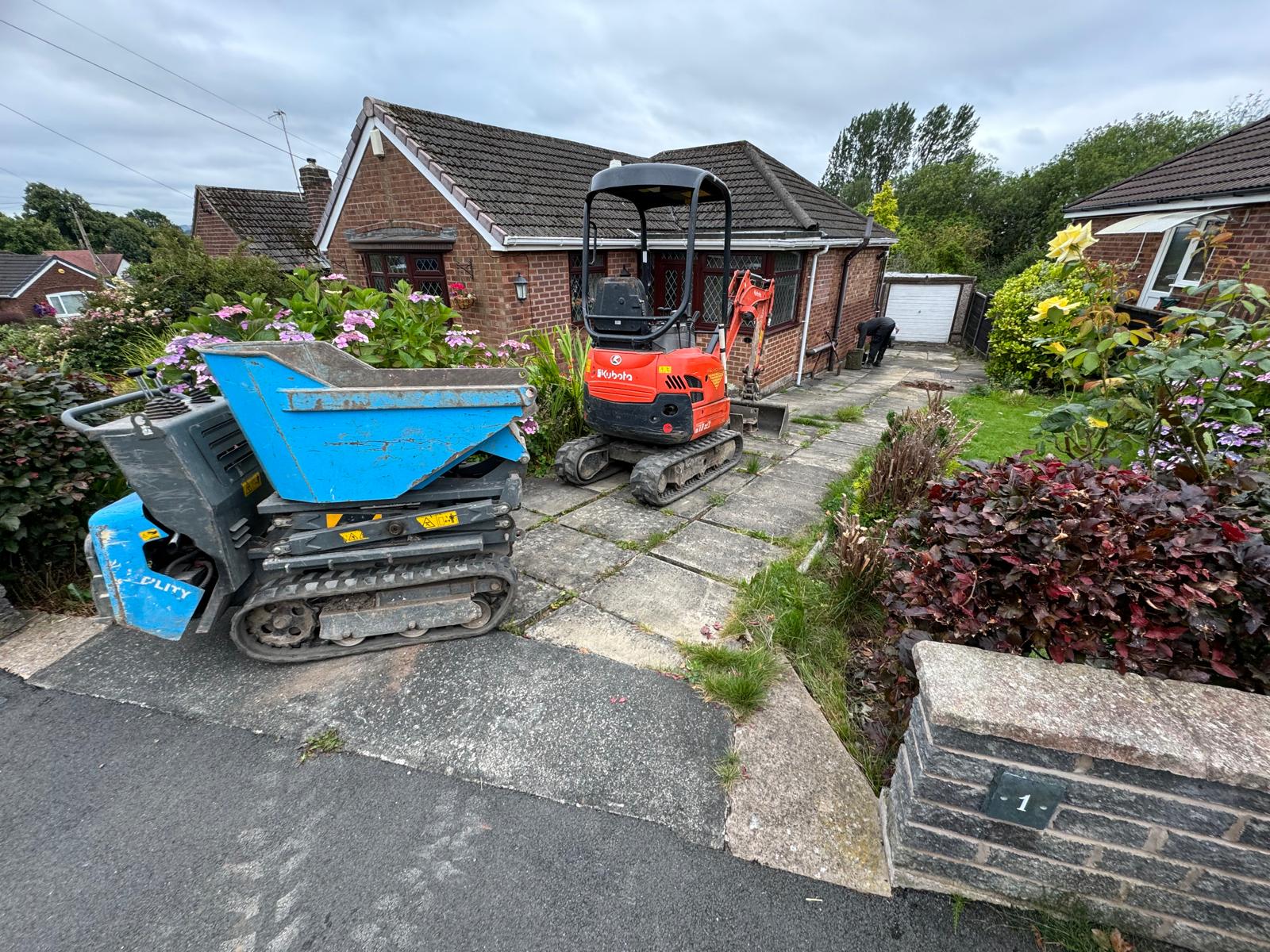 Mini excavator and dumper carrying out driveway groundworks outside a bungalow