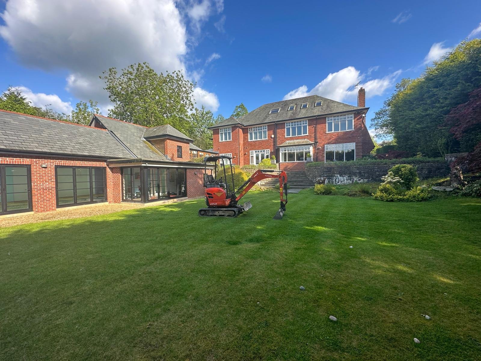 Mini digger starting groundworks on a large rear lawn ahead of an extension rebuild
