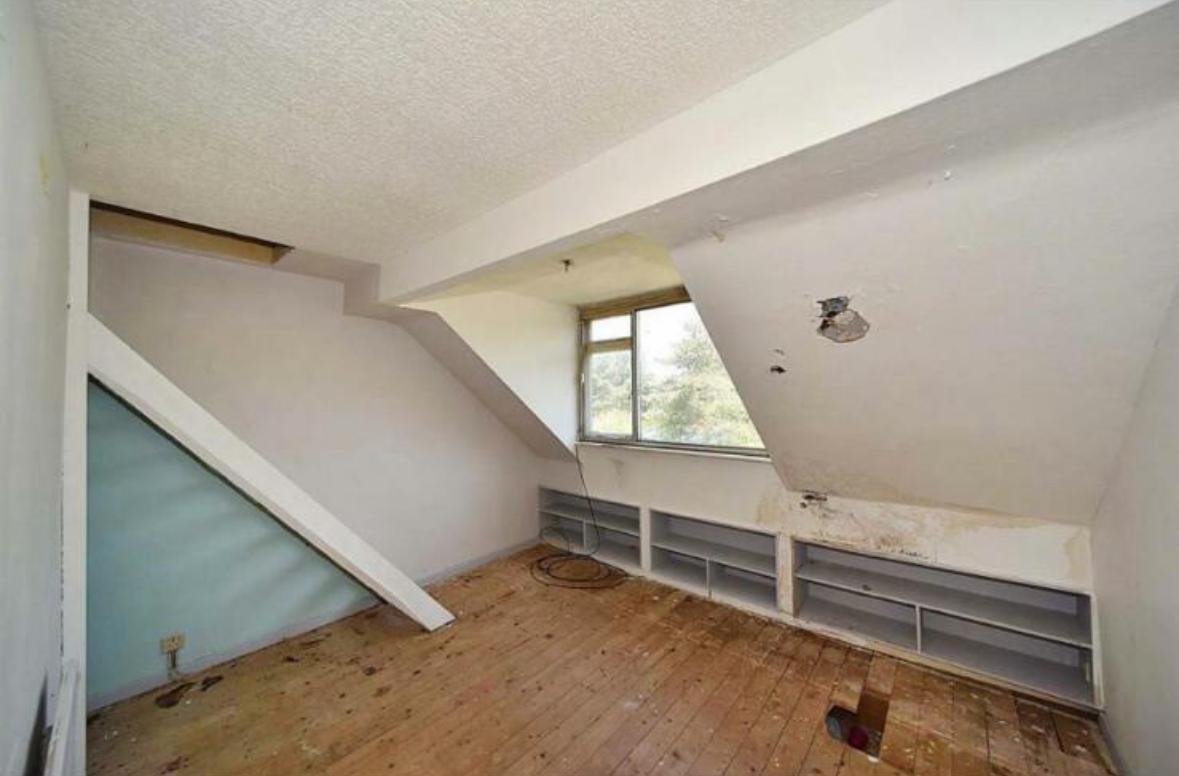 Neglected loft room before renovation with bare floorboards and damaged ceiling