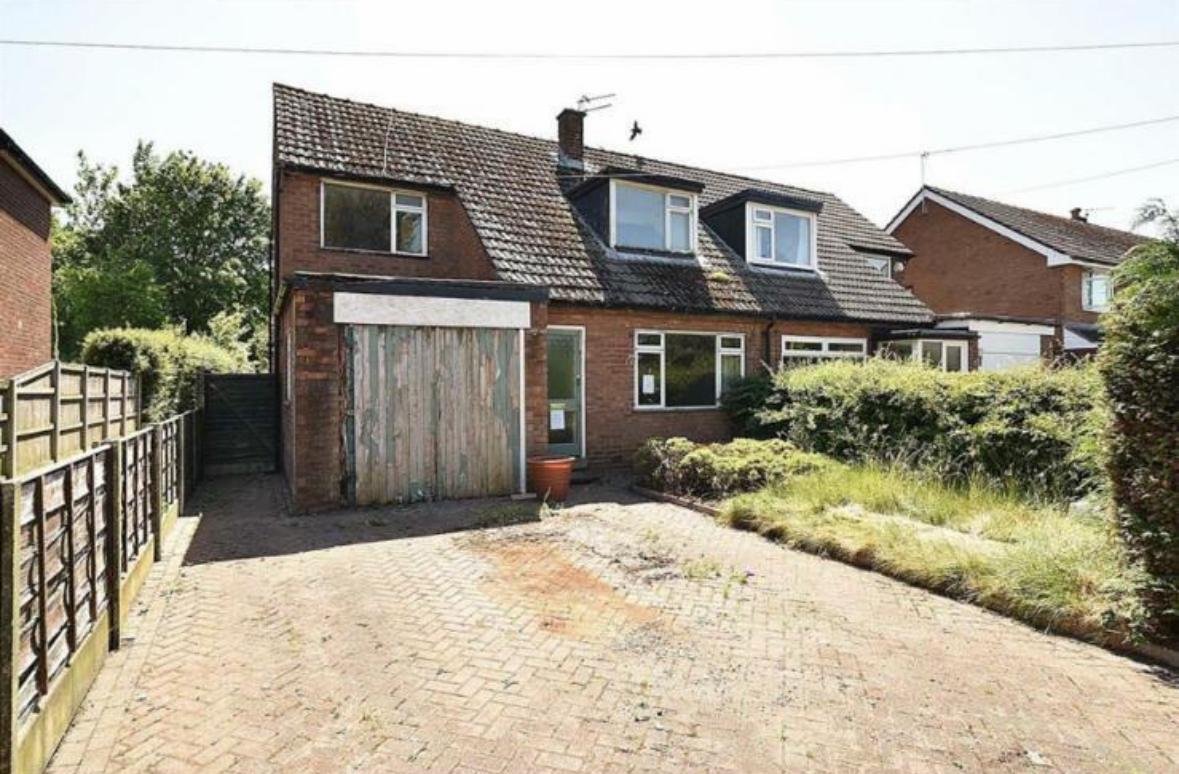 Dated semi-detached house before extension and renovation, with an old garage door and overgrown front garden