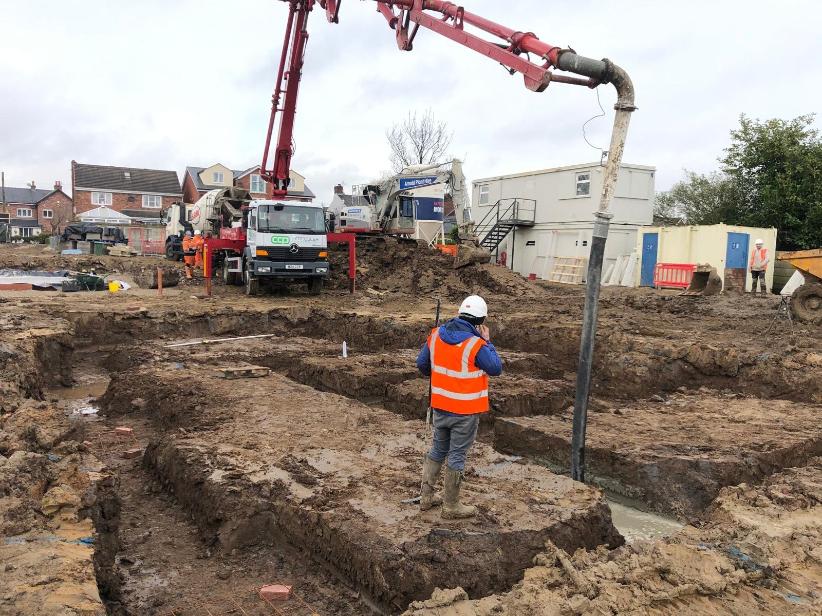 Foundation trenches being dug on a new build site with a concrete pump truck on standby