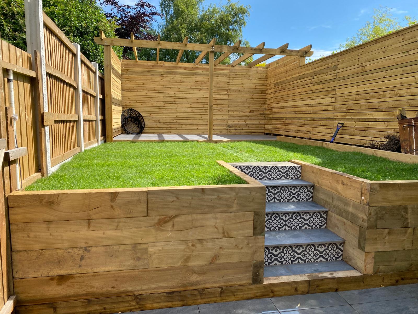 Timber sleeper retaining walls, pergola and patterned tiled steps in a landscaped garden